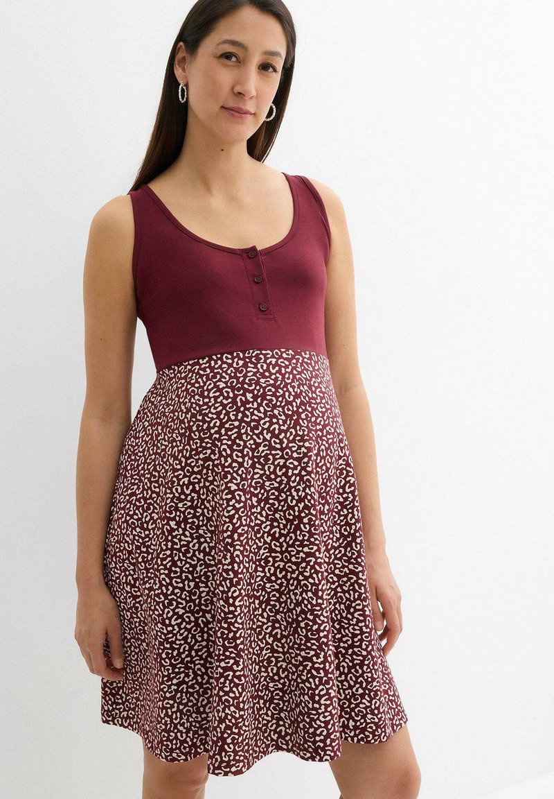 Robe bordeaux avec un corsage ajusté et une jupe à imprimé léopard. Présente un décolleté arrondi et des détails de boutons sur le devant. Tissu doux, coupe évasée.