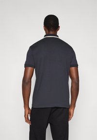 Σκούρο γκρι πόλο με κοντά μανίκια, με λευκή λεπτομέρεια στο γιακά. Κατασκευασμένο από απαλό, ελαφρύ ύφασμα. Απλός σχεδιασμός.