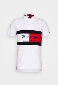Polo shirt blanc avec une rayure horizontale noire et rouge. Comprend un logo brodé et une année d'établissement. Tissu en coton doux, col classique.
