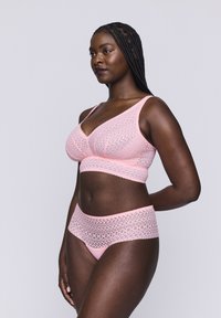 Vaaleanpunainen alusvaatesetti, jossa on pitsisomisteinen bralette ja yhteensopivat korkeavyötäröiset alushousut, joissa on geometrinen kuvio.