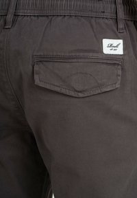 Pantalones oscuros de gris con una cinturilla elástica, que cuentan con un bolsillo trasero con un borde cosido y una etiqueta blanca de marca.