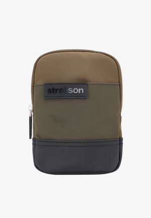 Rechteckiges, mit Reißverschluss versehenes Täschchen aus olivgrünem Stoff, mit einem schwarzen unteren Abschnitt und einem schwarzen Logo-Patch. Glatte Textur, strapazierfähiges Design.