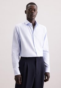 Camicia a quadri blu chiaro e bianco con colletto a punta, maniche lunghe e tessuto liscio, abbinata a pantaloni neri a pieghe.