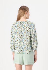 Floral blouse with three-quarter sleeves, featuring a white background, blue and green flower patterns, and a relaxed fit. Paired with green shorts.