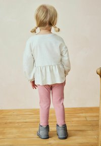 Light gray long-sleeve shirt with a peplum hem, pink leggings with small yellow dots, and gray ankle boots on a wooden floor.