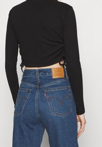 Top de manga larga negro con textura de canalé, combinado con jeans azules de Levi's, que cuentan con un parche de cuero y dos bolsillos traseros con costura curva.