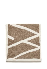 Pătură din lână maro și crem, cu un model geometric în zigzag. Textură moale, cu culori contrastante și o finisare pufoasă.