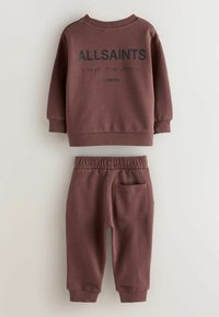 Mørkerød to-delt sæt bestående af en sweatshirt og bukser. Sweatshirten har ribbede manchetter og tekst på bagsiden; bukserne har en elastisk talje og lomme.