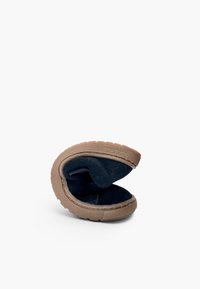 Chaussure en suède bleu foncé pliée avec semelle en caoutchouc souple marron clair sur fond blanc.