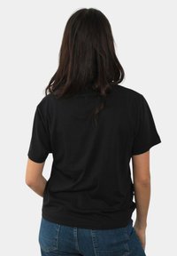 T-shirt nera in cotone con maniche corte, collezione a girocollo e vestibilità rilassata, mostrata da dietro su uno sfondo bianco.