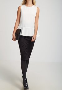 Top blanco sin mangas con peplum combinado con una falda negra ajustada. Botines negros y un clutch negro añaden contraste al conjunto.