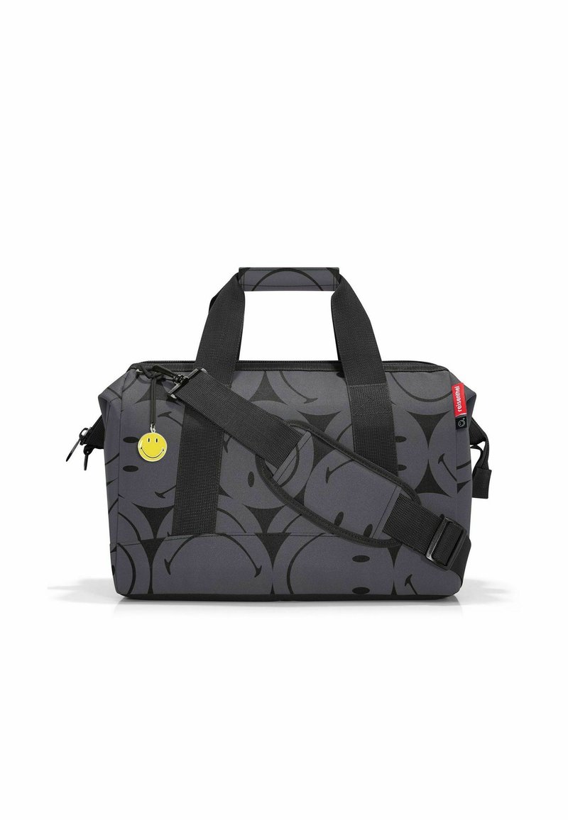 Borsa da viaggio in tessuto grigio con motivo a faccina sorridente nera, manici in webbing neri, tracolla regolabile e dettaglio di portachiavi a faccina sorridente gialla.