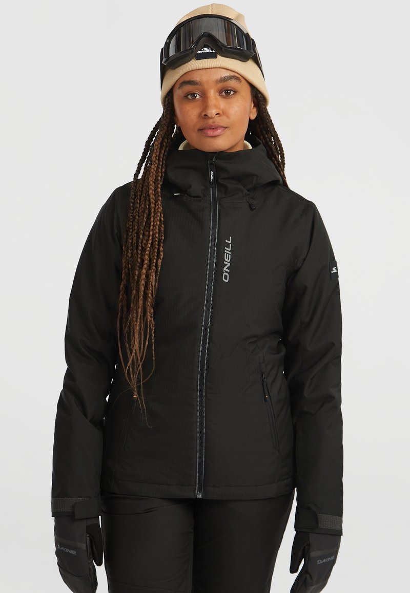 Veste de ski noire avec fermeture éclair sur le devant et col haut. Présente un logo sur la poitrine, des poches zippées et un tissu texturé. Associée à des gants noirs.