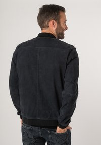 Marineblauwe suède bomberjack met een geribbeld kraag en mouwen. Heeft een strak ontwerp en een rechte rugnaad. Subtiele textuur zichtbaar.