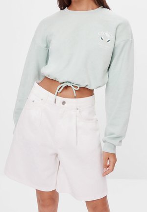 Sweatshirt cropped vert menthe avec des détails de cordon de serrage, associé à un short blanc taille haute. Le sweatshirt présente le logo "Georgia" à l'avant.