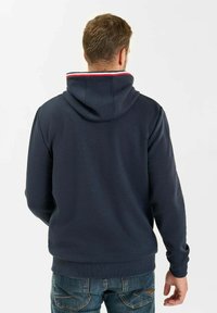 Sudadera azul marino con un bolsillo canguro frontal, puños acanalados y un acento a rayas rojas y blancas en el interior de la capucha. Textura suave.