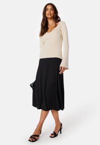 Beige geribbelde langemouwen top gecombineerd met een vloeiende zwarte midi rok. Zwarte gespen hakken maken de look compleet. Geen noemenswaardige patronen of accenten.