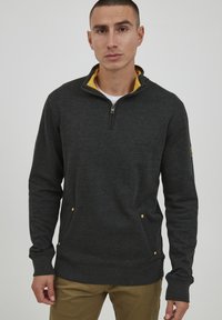 Sudadera de forro polar gris oscuro con media cremallera y cuello amarillo. Presenta bolsillos laterales con acentos amarillos y puños acanalados. Textura suave.