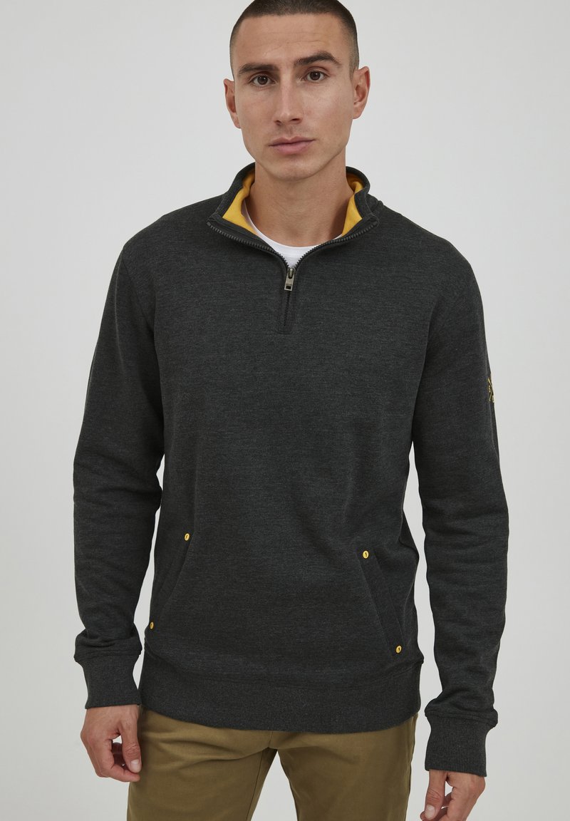 Pullover in pile grigio scuro con zip a quarto e colletto giallo. Caratterizzato da tasche laterali con accenti gialli e polsini a costine. Texture liscia.