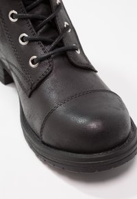 Botte noire en cuir à lacets avec œillets en métal, bout rond et semelle en caoutchouc épaisse sur fond blanc.