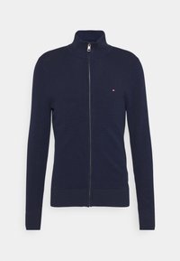 Mörkblå zip-up tröja med hög krage, stickad struktur, ribbade cuffs och nederkant. Har ett litet logomärke på vänstra bröstet.