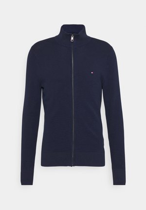 Maglione zip-up navy con colletto alto, texture lavorata a maglia, polsini e orlo a coste. Presenta un piccolo logo ricamato sul lato sinistro del petto.