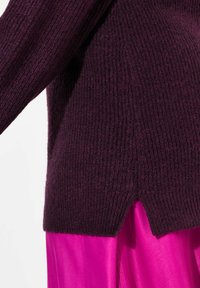 Maglione viola a righe con design cropped, caratterizzato da una fessura laterale, indossato sopra un capo in satin rosa brillante. Texture morbida, vestibilità comoda.