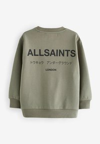 Maslinasto zelena dukserica s rebrastim manžetama i donjim rubom. Ima veliki crni natpis "ALLSAINTS" i "LONDON" na leđima. Minimalistički dizajn.