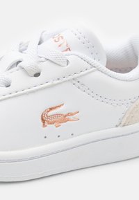 Hvite lær sneakers med en teksturert rosegull-logo, jevn overflate, rund tå og matchende hvite snørebånd. Har en myk innersåle.