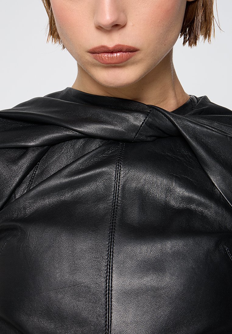 Czarna skórzana bluzka o gładkiej fakturze, z twistowym wzorem przy dekolcie i widocznymi detalami przeszyć. Zbliżenie na odzież.