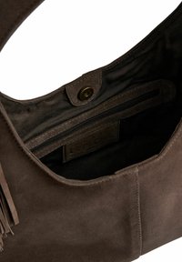 Braune Wildleder-Handtasche mit glatter Textur, ausgestattet mit einem inneren Reißverschlussfach und einem magnetischen Druckverschluss. Mit Fransenakzenten verziert.