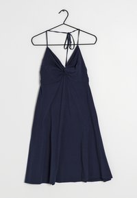 Mörkblå ärmlös klänning med spaghettistilar och rynkodetalj vid bröstet, hängande på en svart galge mot en vit bakgrund.