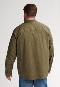 Camicia a maniche lunghe da uomo in verde oliva con un sottile motivo geometrico. Presenta un colletto classico e polsini con bottoni. Tessuto in misto cotone.