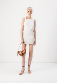 White sleeveless top with square neckline, paired with a light patterned mini skirt and a brown textured handbag, worn with neutral strappy heels.