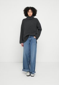 Hiilipaita neulottu poolokaulusneule yhdistettynä leveälahkeisiin sinisiin farkkuihin ja valkoisiin kenkiin. Rentoutunut istuvuus, paksu resorikaulus ja käännetyt hihansuut.