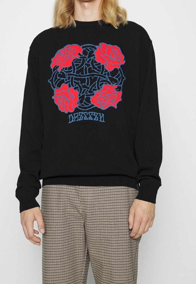 Pull noir avec un graphique proéminent de roses rouges et des détails bleus. Poignets et ourlet côtelés, coupe décontractée. Texture légère.