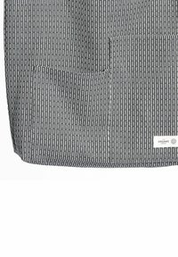 Čierno-biela pruhovaná látka s textúrovaným tkaním, vybavená dvomi prednými vreckami a štítkom označeným "The Organic Company".