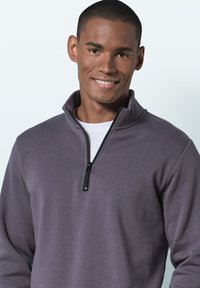 Gray zip-up sweatshirt with a high collar, made of soft fabric. Features a black zipper and a white shirt underneath.