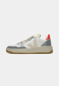 Low-top sneaker with beige suede accents, metallic silver overlays, white base, gum sole, and red heel tab with branding.