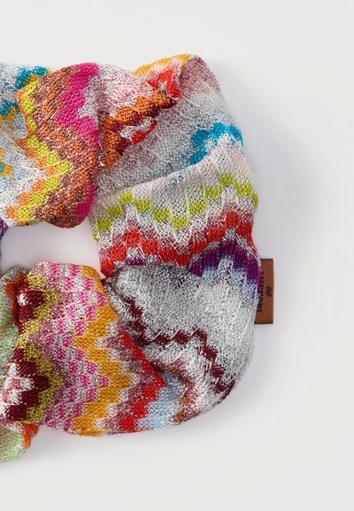 Écharpe tricotée multicolore avec des motifs en zigzag rose, orange, rouge, jaune, vert, bleu, violet et argent sur fond blanc.