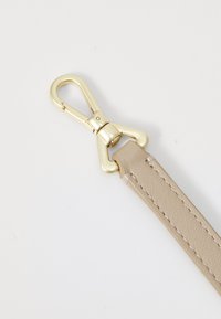 Cinturino in pelle beige con moschettone in metallo dorato, caratterizzato da una superficie testurizzata e dettagli di cucitura lungo i bordi.