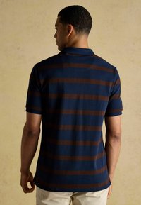 Tengerészeti póló, vízszintes barna csíkokkal, rövid ujjakkal és bordázott gallérral. Pamut anyag, sima textúrával.