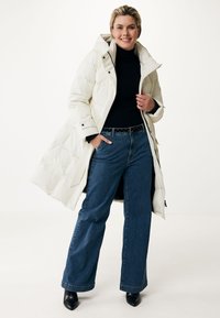 Cappotto lungo imbottito di colore bianco sporco, dotato di cappuccio, chiusura con zip e tasche laterali. Abbinato a jeans a gamba larga in denim scuro e tacchi neri.