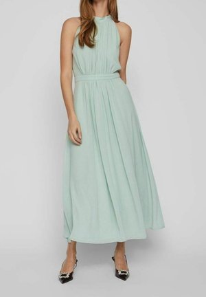Woman wearing a sleeveless, light blue halter neck midi dress with pleats, paired with black pointed-toe heels embellished with rhinestones.