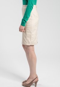 Beige pennkjol med en slät textur och en sidoflik, tillsammans med en grön långärmad blus och beige högklackade skor.