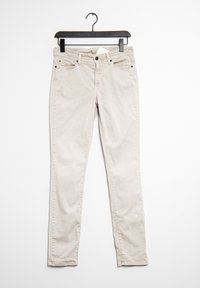 Jeans beige colgados de una percha negra. Incluye cinco bolsillos, una cremallera y una textura sutil en la tela de algodón.