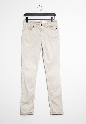 Béžové džíny visící na černém ramínku. Obsahují pět kapes, zip a jemnou strukturu v bavlněné tkanině.