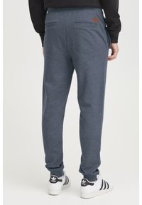 Grå sweatpants med en afslappet pasform, der har to baglommer og et lille brunt mærke. Stoffet har en blød, struktureret overflade.