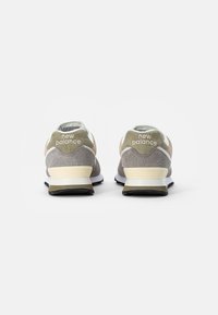Baskets New Balance beige et grises en mélange de suède et de mesh, avec un logo blanc sur le talon, une semelle coussinée et une semelle extérieure noire.