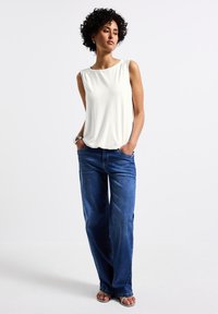 Vit ärmlös topp med subtila veck, kombinerad med lösa blå denimjeans. Rak benkropp, medelhög tvätt och en avslappnad passform. Silverdetaljer synliga.
